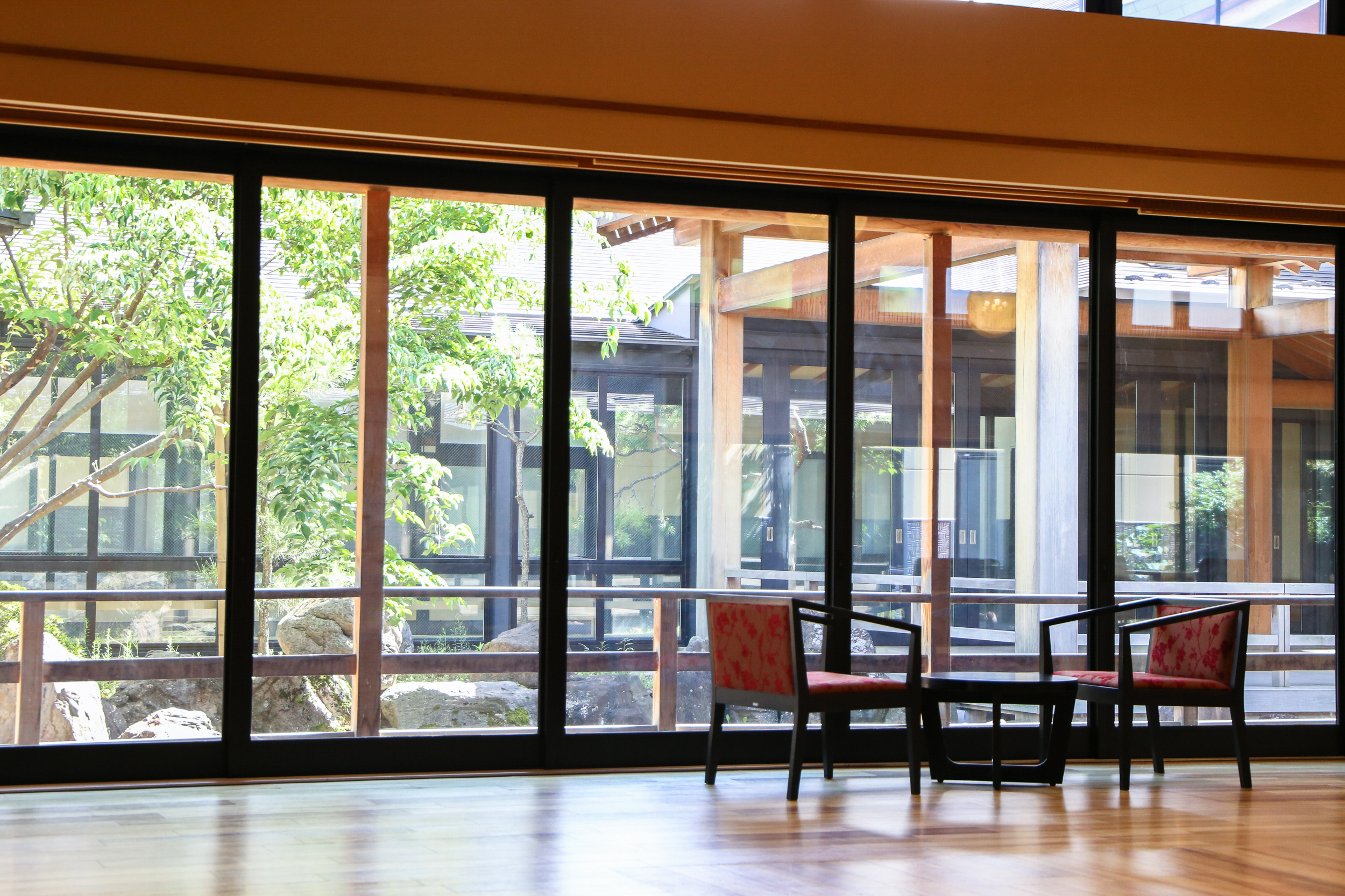施設内の椅子と机と窓から見える庭園の風景写真