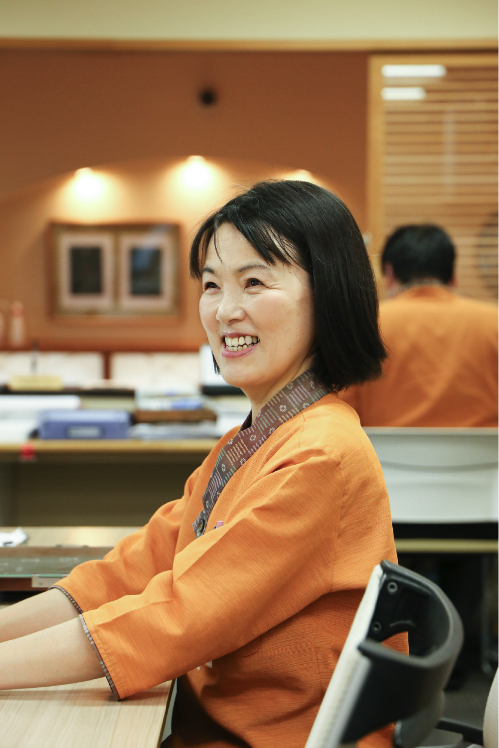 オレンジ色の服を着た笑顔の女性職員の写真
